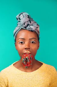 Portrait of woman carrying necklace in mouth against blue background