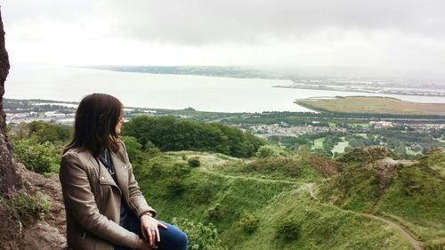 Woman sitting on rock looking at scenic view of sea