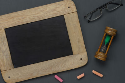 Directly above shot of wooden slate with chalks and hourglass on table