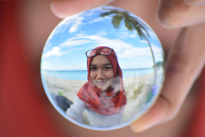 Cropped image of woman wearing red hijab reflecting on crystal ball at beach