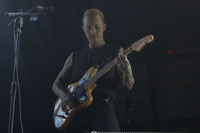 Young man playing guitar against black background