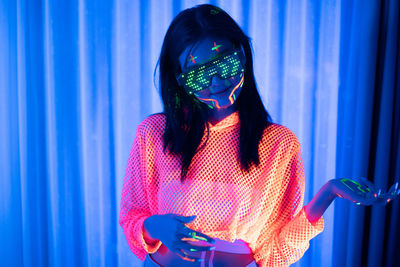 Midsection of woman holding umbrella standing against illuminated wall