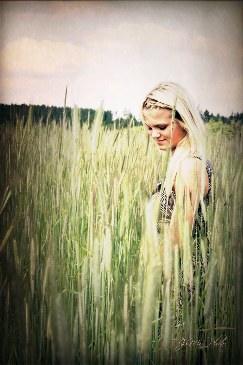 field, grass, lifestyles, person, standing, leisure activity, casual clothing, sky, three quarter length, young adult, front view, holding, plant, landscape, rural scene, grassy, portrait, full length