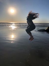 Woman jumping at beach against sky during sunset