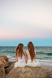 Rear view of woman sitting on beach against sky