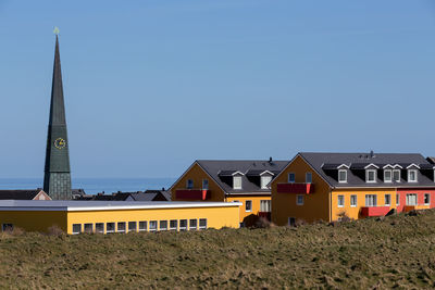 Houses by buildings against clear blue sky