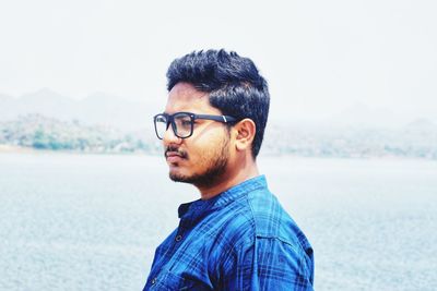 Close-up of young man wearing eyeglasses against sea at beach