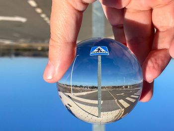 Cropped hand holding crystal ball with reflection against road sign