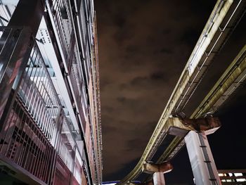 Low angle view of illuminated bridge against buildings at night