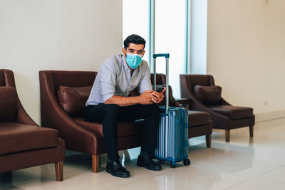 Portrait of man wearing mask sitting on chair at hotel