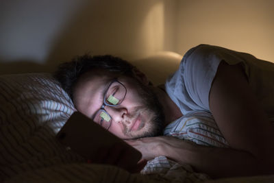 Adult sleepy man with glasses surfing in web before dreaming. social media addiction