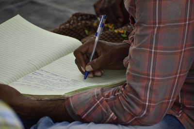 Midsection of man writing in book