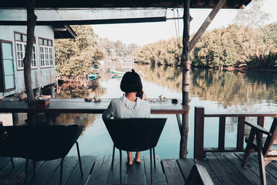 Rear view of woman sitting on table by lake