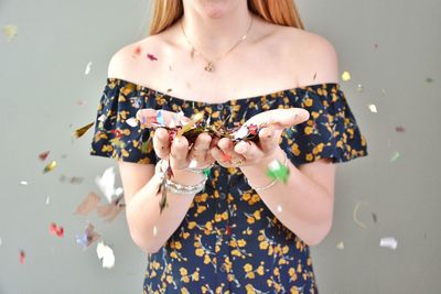 Midsection of woman blowing confetti against gray background