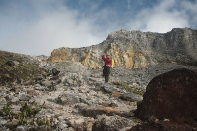 Low angle view of man on rocky mountain against cloudy sky