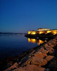 Sea by illuminated buildings against clear blue sky