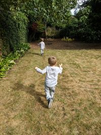Rear view of twin boys running on grass against trees