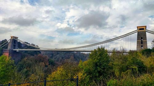 Low angle view of suspension bridge against cloudy sky