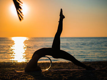 Silhouette woman doing yoga at beach against sky