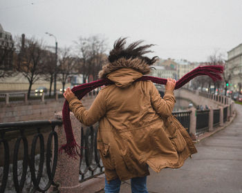 Rear view of woman with warm cloth holding scarf in city