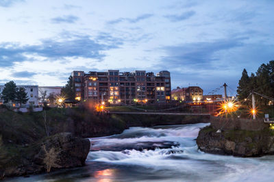 Illuminated city by sea against sky at night