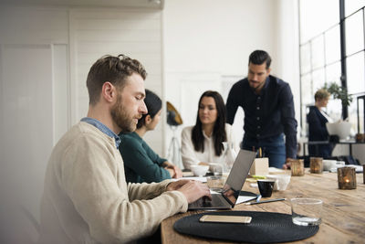 Businessman using laptop while coworkers discussing at meeting in office