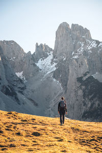 Rear view of man walking on snowcapped mountain against sky