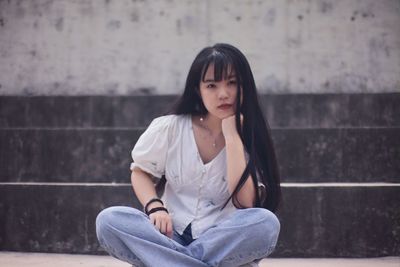 Beautiful young woman sitting against wall