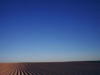 Scenic view of plowed field against clear blue sky