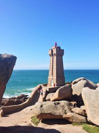 Lighthouse by sea against clear blue sky