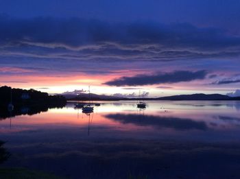 Scenic view of loch  against dramatic sky during sunset