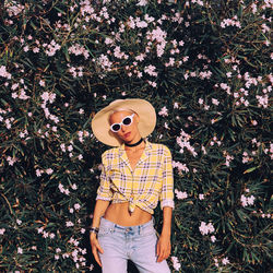 Portrait of woman wearing hat standing against flowering plants