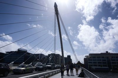 People on bridge in city against cloudy sky