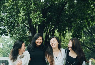 Cheerful female friends standing against trees