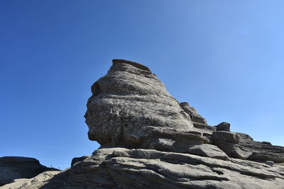 Low angle view of rock formation against clear blue sky