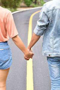 Midsection of couple holding hands while standing on road