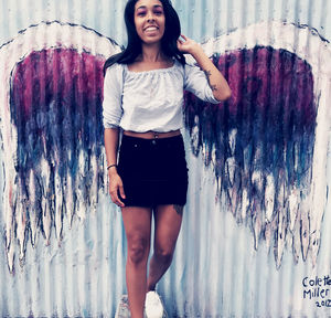 Portrait of smiling young woman standing against wall