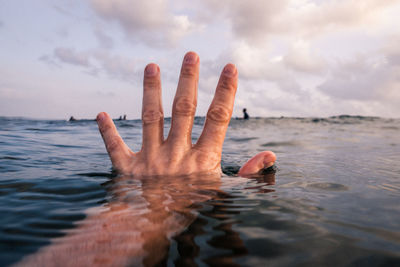 Person hand in sea against sky