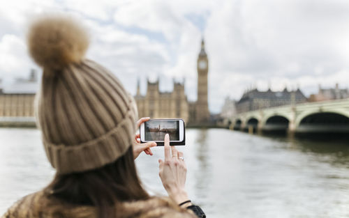 Uk, london, back view of young woman taking picture of westminster parliament