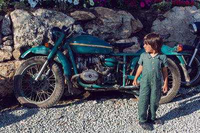 Child boy in a green jumpsuit walks among old motorcycle in the summer