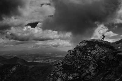 Distant view of hiker standing on rocky mountain against cloudy sky