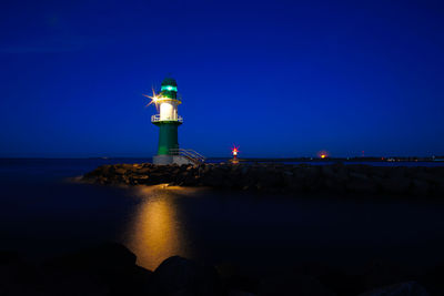 Lighthouse by sea against sky at night