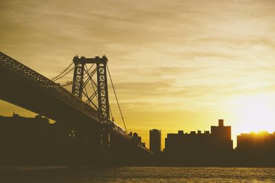 Silhouette bridge over river against sky during sunset