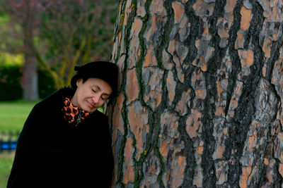 Smiling woman leaning on tree trunk