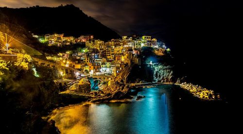 Illuminated buildings by sea against sky at night