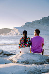 Rear view of couple sitting on beach against sea