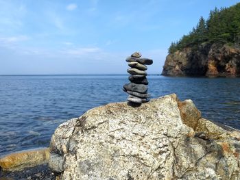 Stack of stones on rock by sea against sky