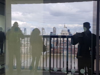 Rear view of people standing by railing in city against sky