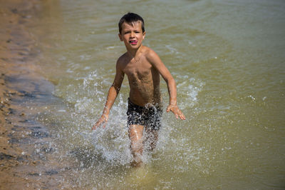 Playful shirtless boy running on shore at beach