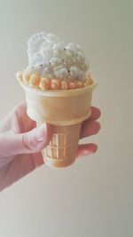 Close-up of hand holding ice cream cone against white background